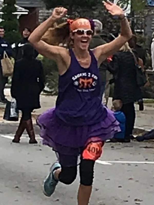 Dr. Gelnett running a town race in a purple tutu with her arms in the air